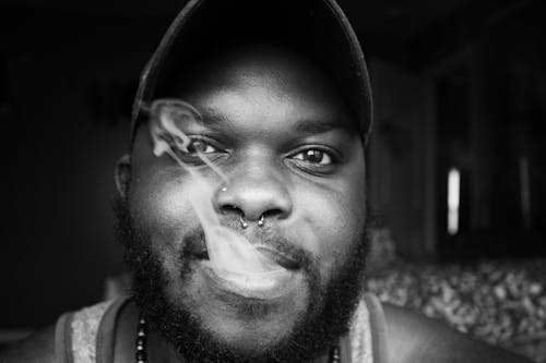 Grayscale Photo of a Man With a Nose Ring Exhaling Smoke