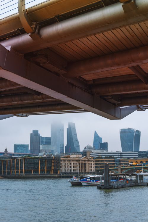 Free View of London's iconic skyline from beneath a bridge with modern skyscrapers and the River Thames. Stock Photo