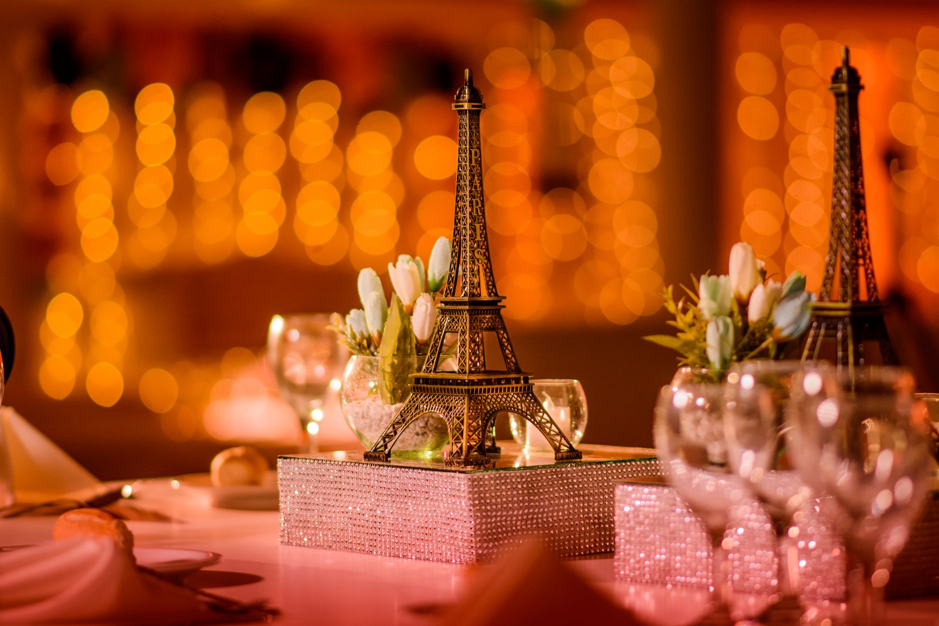 Prom Theme Ideas Students Will Get Behind Chic table setting featuring a decorative Eiffel Tower model with glowing bokeh lights.