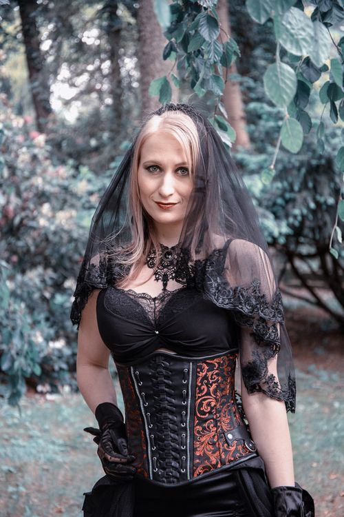 Free Elegant woman in gothic attire posing outdoors with a black lace veil. Stock Photo
