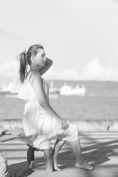 Free Relaxed woman sitting on wooden bench on beach Stock Photo