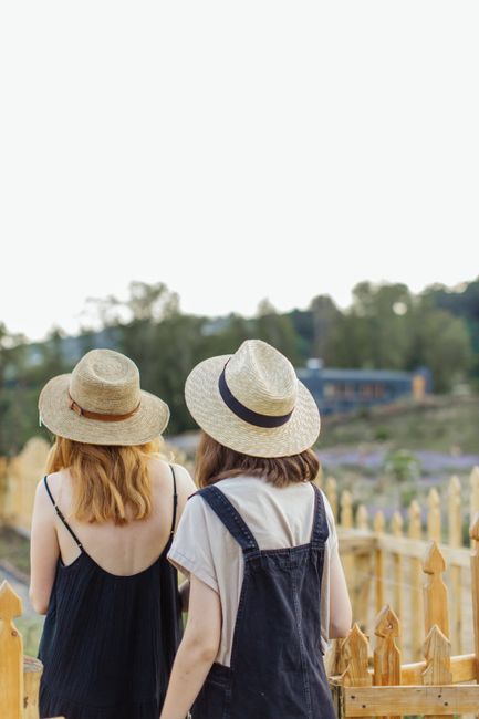 Two women in straw hats enjoy a peaceful walk by a wooden fence in the countryside.