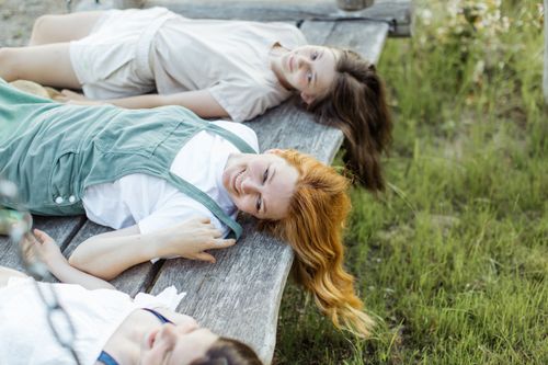 Free Three teenage friends enjoy a relaxing moment on a wooden bench in a summer meadow. Stock Photo