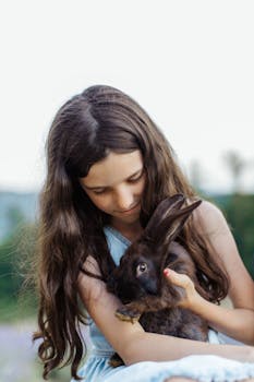 一位年轻女孩留着长发，在户外抱着一只棕色兔子