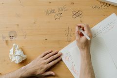 A person drawing on a wooden desk covered in creative doodles and handwritten notes.