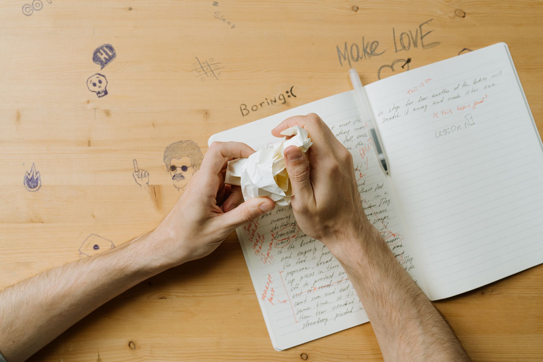 Hands crumpling paper over a notebook showing creative frustration at a writing desk.
