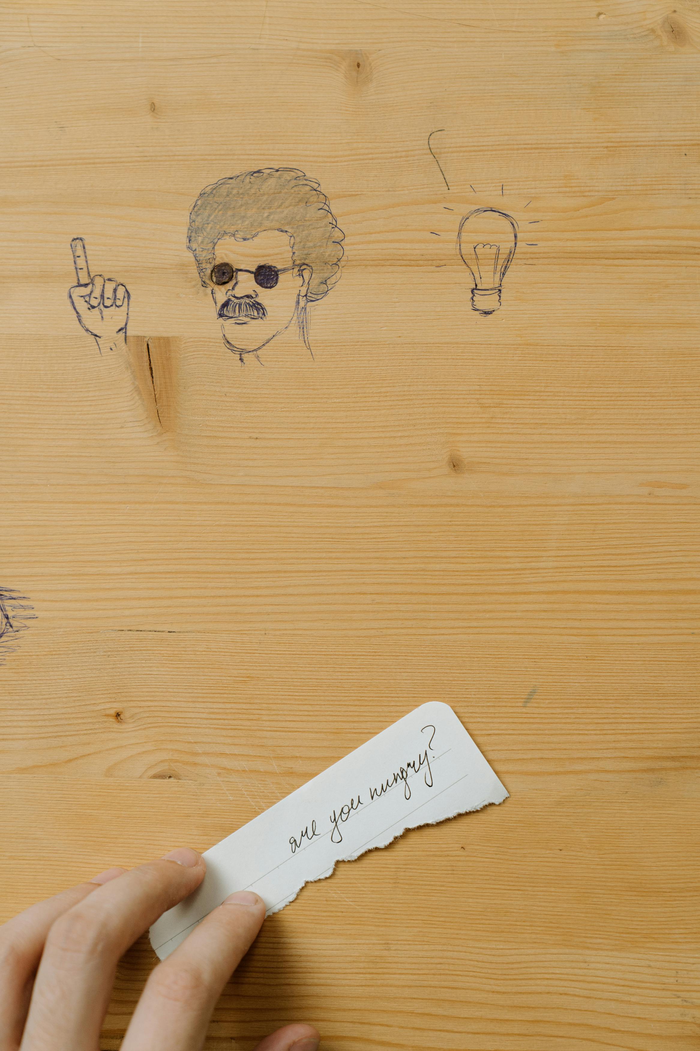 Close-up of doodles on a wooden desk with a hand holding a note.