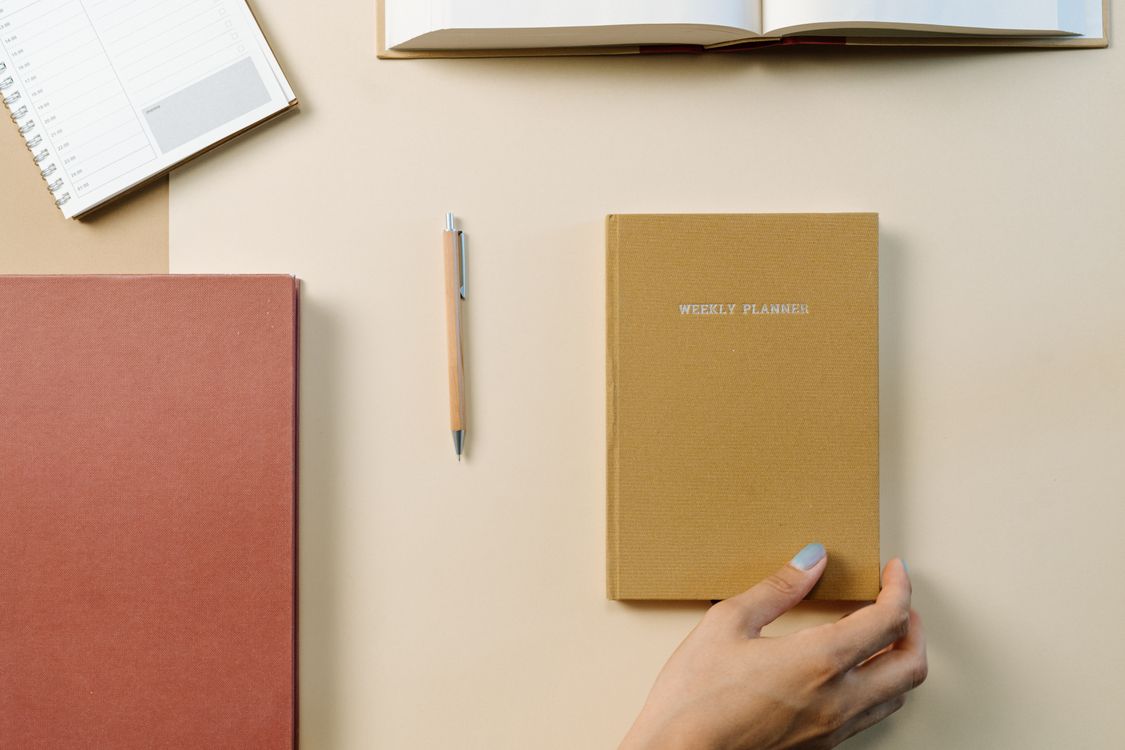 Weekly planner, notebooks and pencil on a warm neutral desk Weekly planner, notebooks and pencil on a warm neutral desk