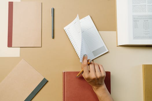 Top view of a hand flipping diary pages on a neat office desk with books and pens.