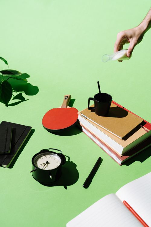 Free Artistic composition featuring books, clock, ping pong paddle, and coffee on a bright green background. Stock Photo