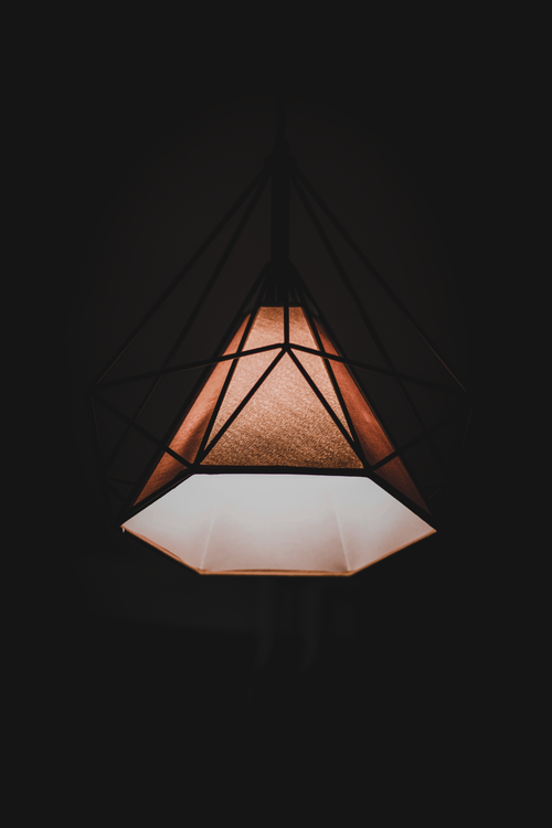 Free Close-up of a geometric pendant light with a warm glow against a dark background. Stock Photo