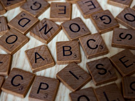 Scattered wooden Scrabble tiles showcasing letters and typography on light wooden surface.