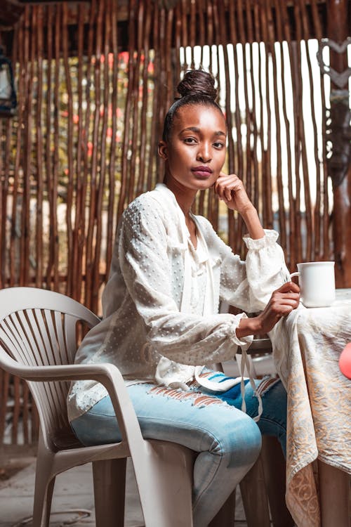 Side view low angle of pensive young African American female leaning on hand while having tea in cafe