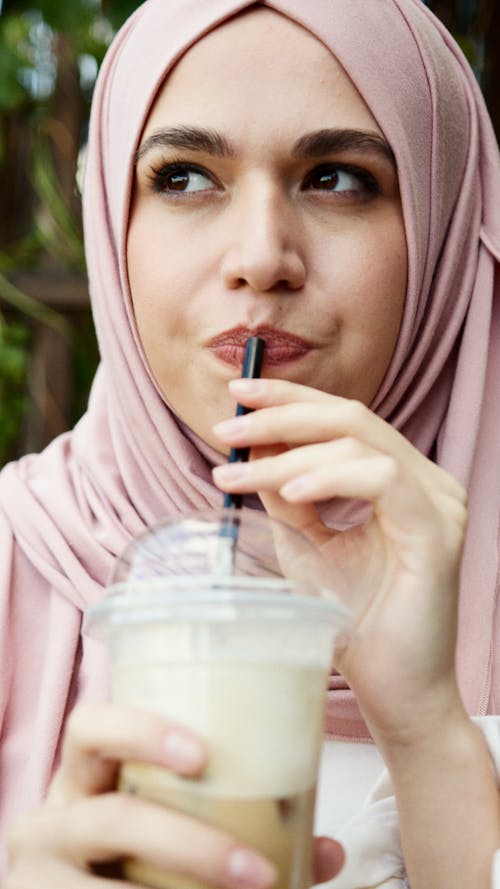 Woman in Pink Hijab Drinking from a Straw