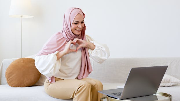 Woman in hijab on a video call makes a heart gesture, expressing affection and connection.
