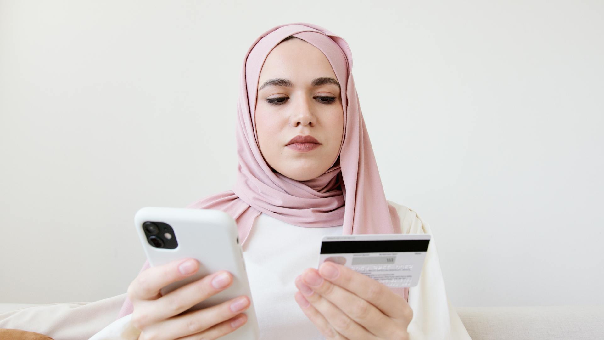 Woman in Pink Hijab Holding White Mobile Phone and Credit Card