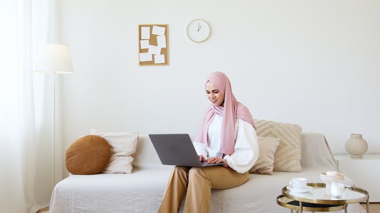 Woman In Pink Hijab Sitting On Couch While Using Gray Laptop