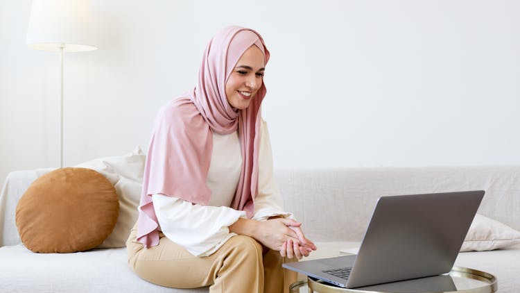 Woman In Pink Hijab Sitting On White Sofa While Using Gray Laptop