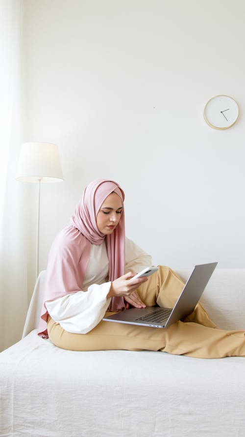 Free Woman in Pink Hijab Using Laptop and White Smartphone Stock Photo