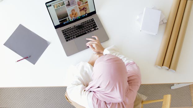 Top view of a businesswoman in a hijab working on a laptop at a modern workspace.