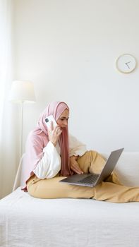 一位戴着头巾的女商人正在家庭办公室里用笔记本电脑打电话