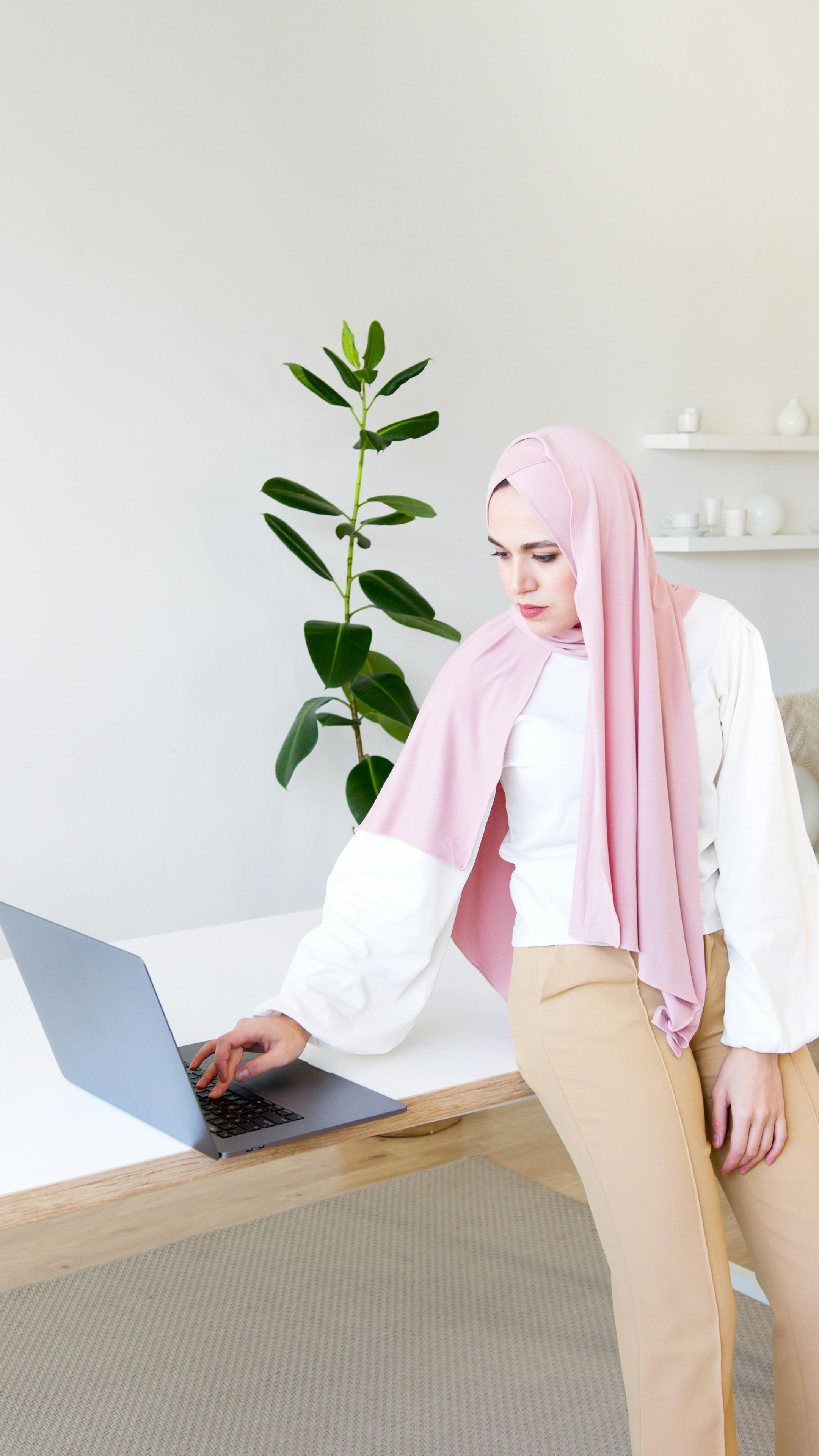 Businesswoman in hijab using a laptop in a stylish home office setting with plants.