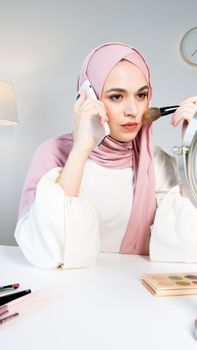 一名戴着头巾的穆斯林妇女在室内拿着手机化妆