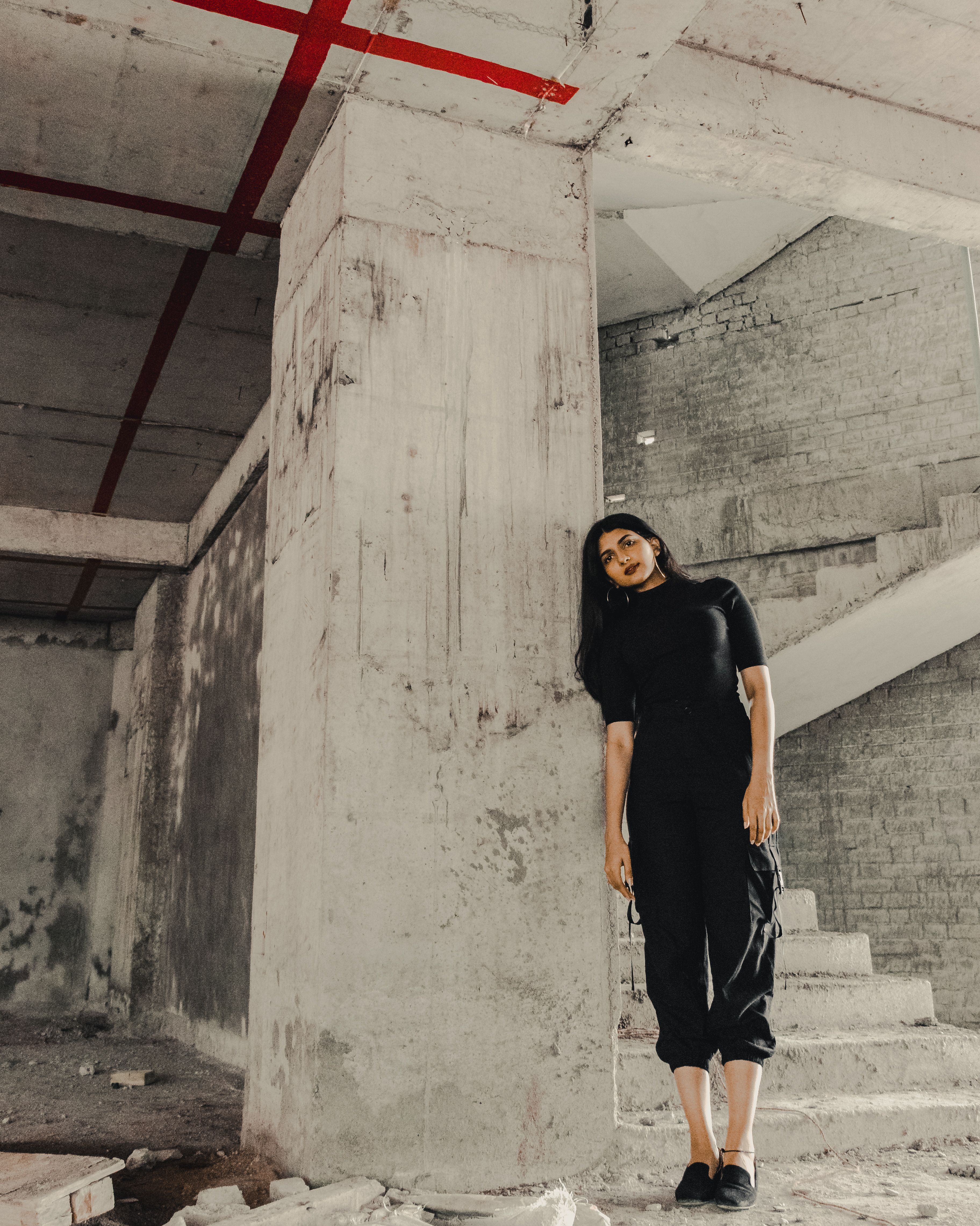 一名妇女靠在一栋未完工建筑的混凝土柱子上，周围有楼梯和碎片