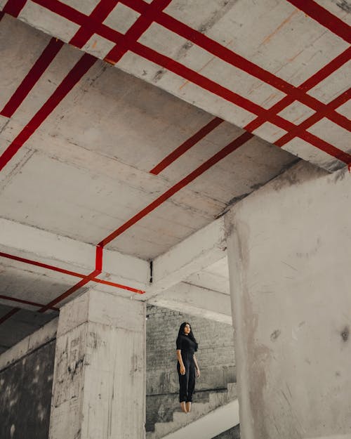 Free Young Woman in Black Clothes Standing on the Stairs in Abandoned Building with Red Lines on the Ceiling Stock Photo