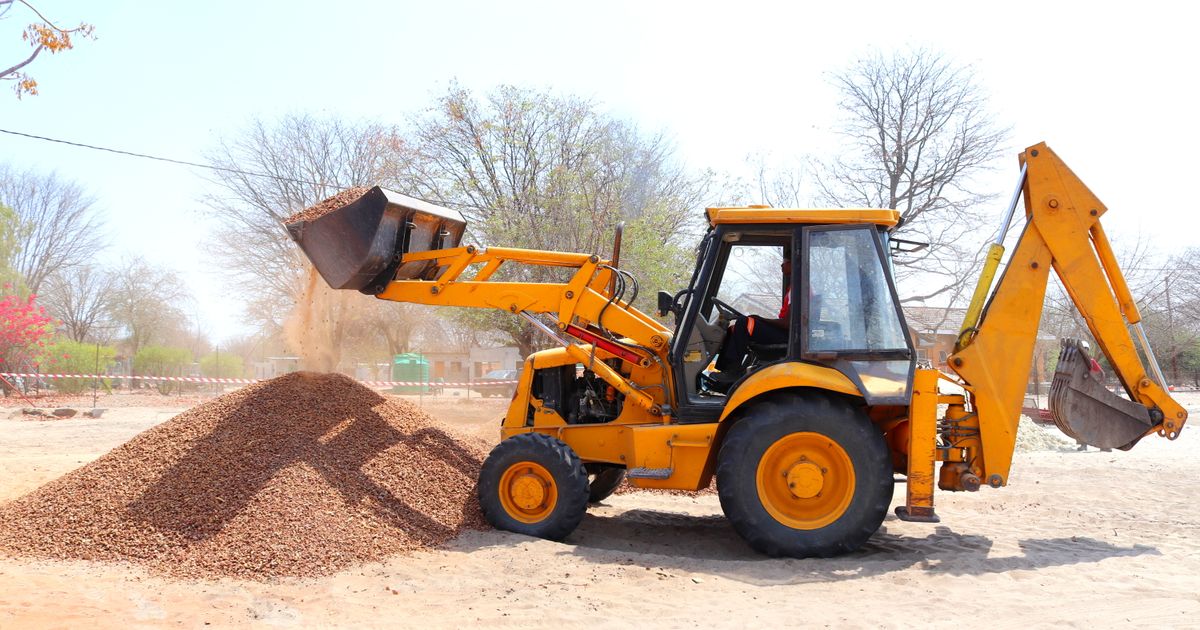 Yellow excavator moving gravel at an outdoor construction site — the earthmoving work that small dumper trucks support on restricted-access sites