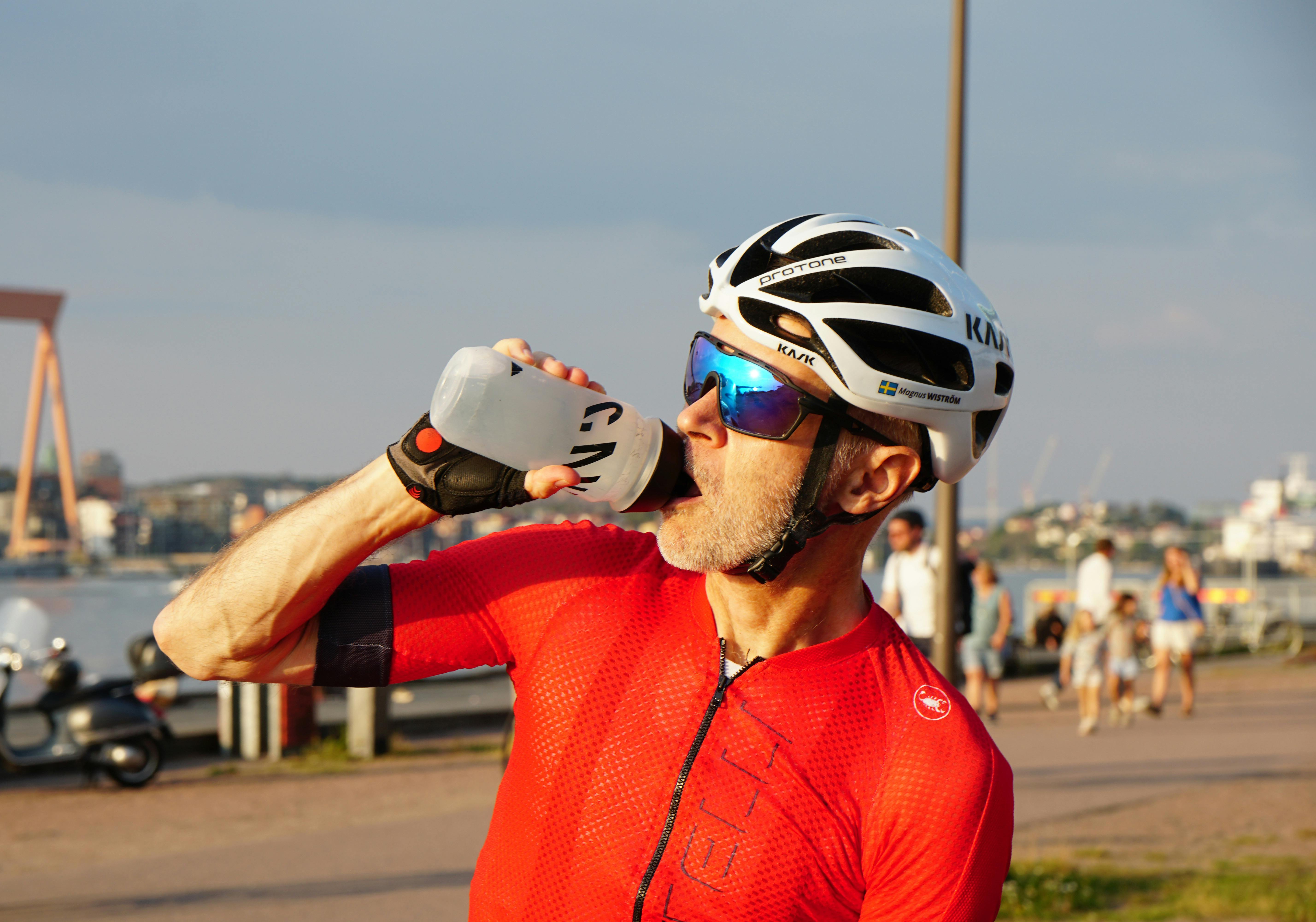 Male cyclist in red jersey drinking water outdoors, Gothenburg, Sweden.