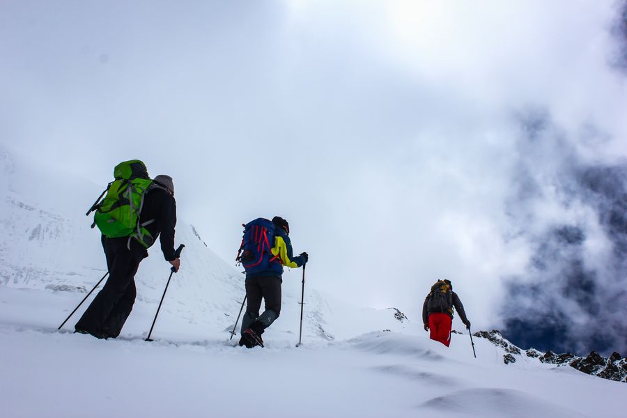 Hikers climbing a snowy ridge on a cloudy day
