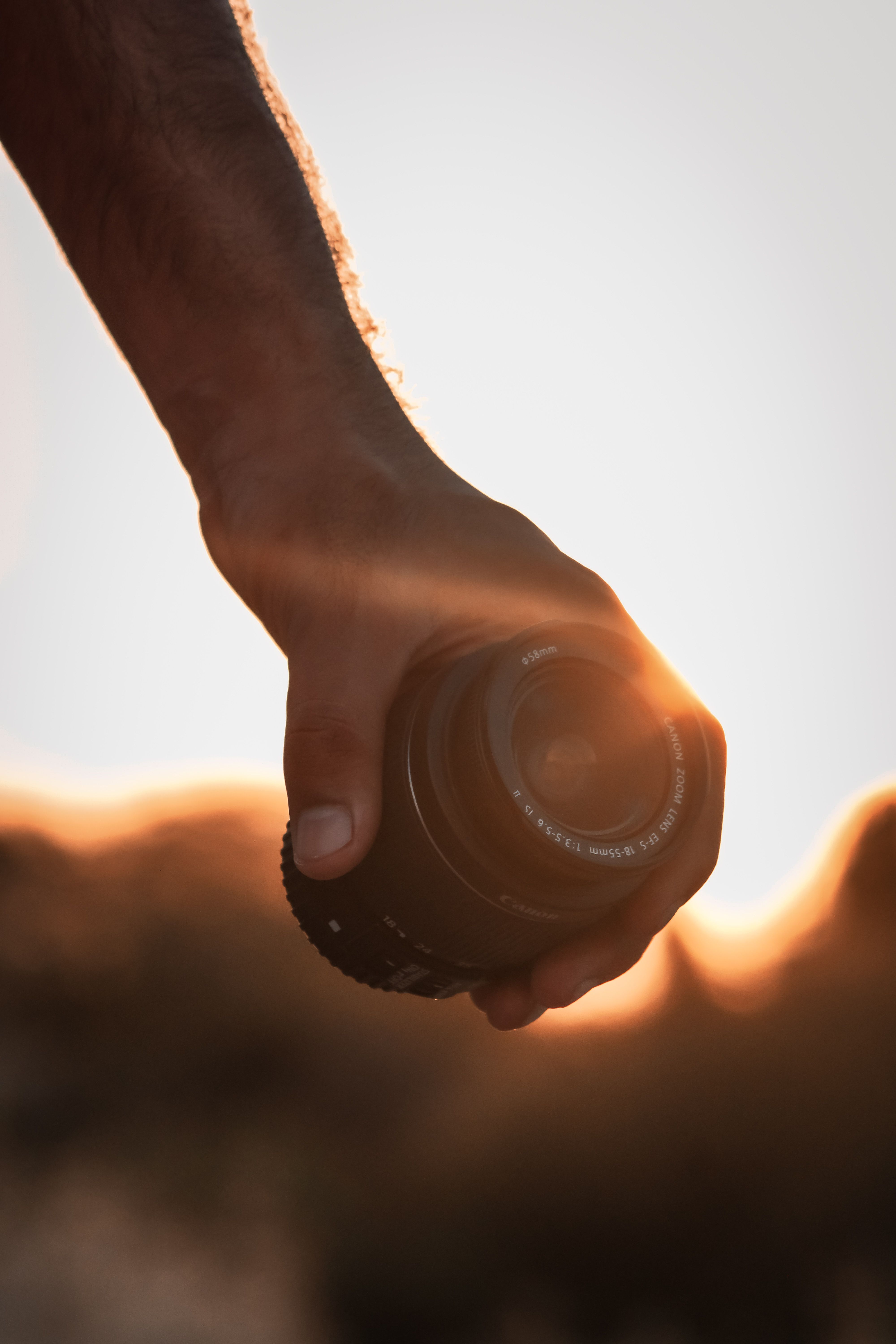 Free Artistic silhouette of a hand holding a camera lens against a sunset backdrop, creating a dramatic visual effect. Stock Photo