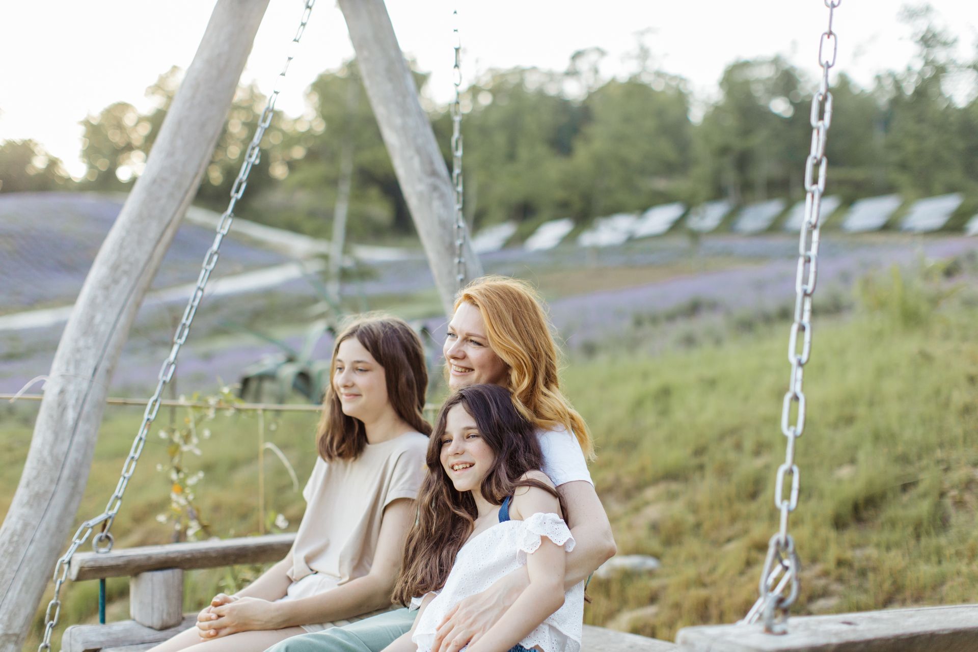 Three smiling females enjoying a peaceful moment on an outdoor swing surrounded by nature.