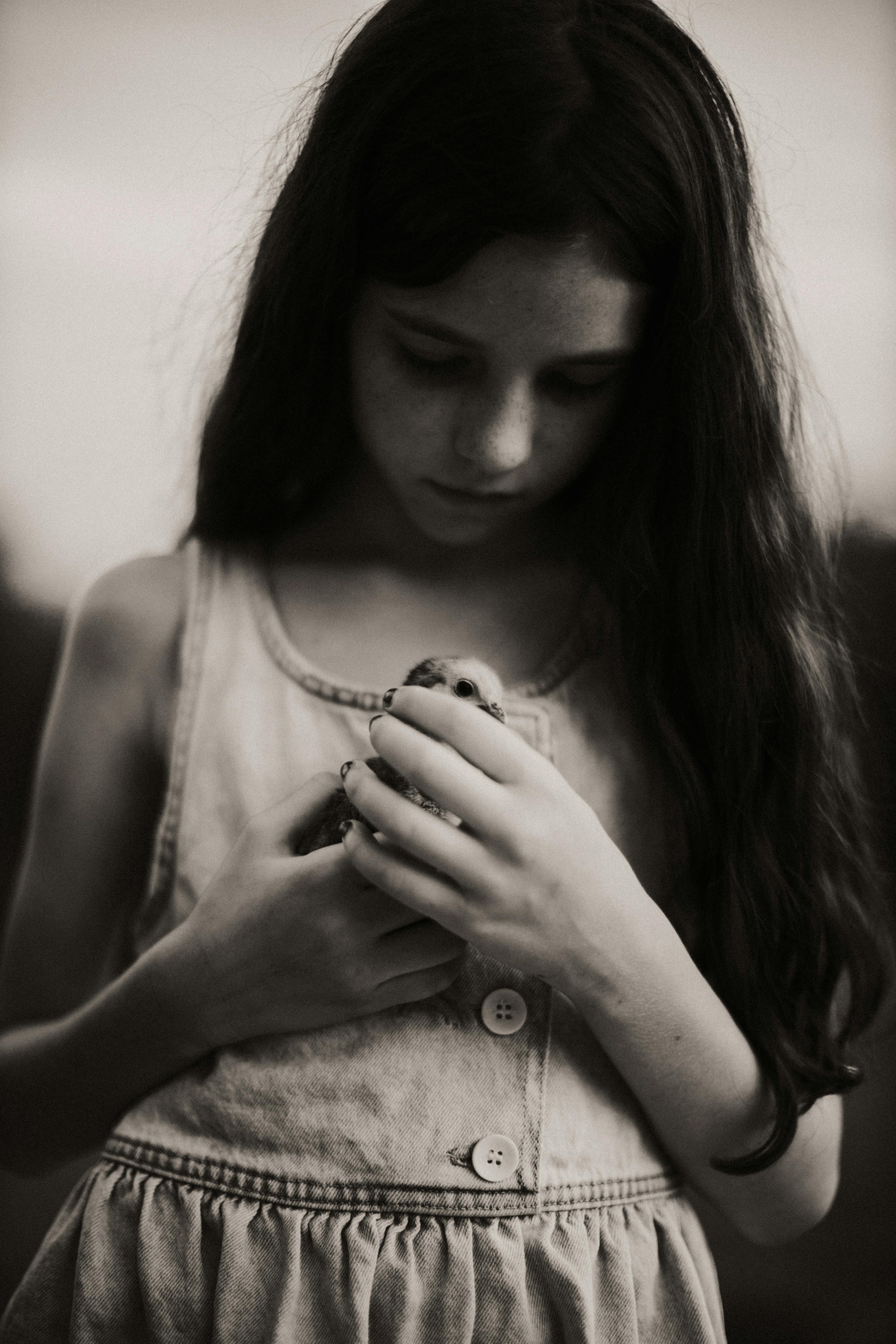 Black and white photo of a girl holding a bird, evoking calmness.