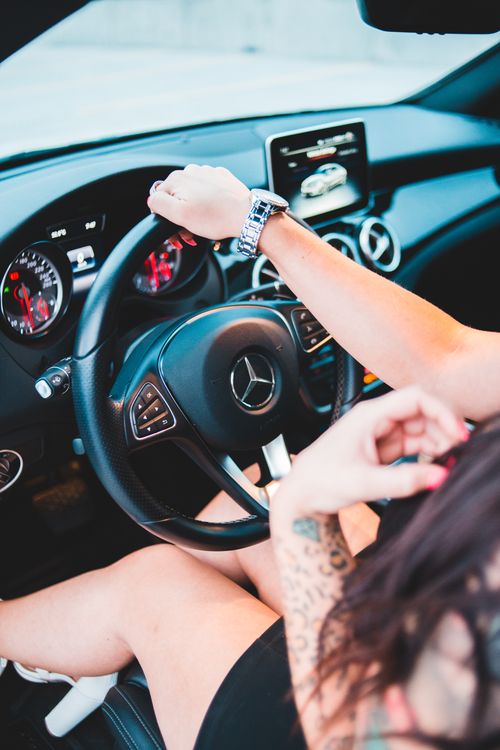 Free Faceless female in short black dress and tattoo on arms driving luxury automobile in daytime Stock Photo