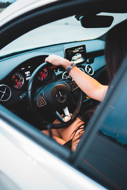 Free Unrecognizable female with dark hair in dress holding big steering wheel while driving expensive white car in daylight Stock Photo