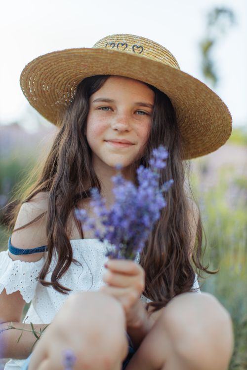 Free A young girl wearing a straw hat holds a bouquet of lavender. It's a sunny day. Stock Photo