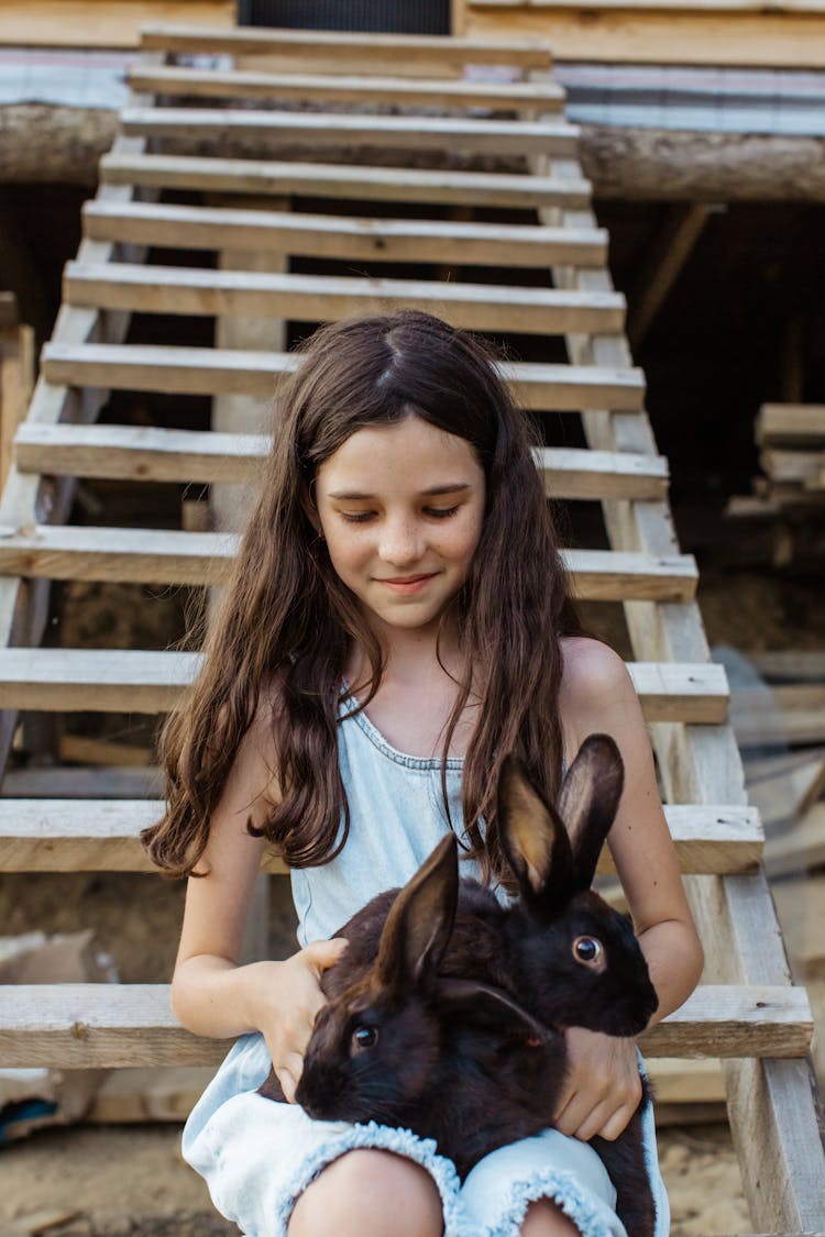 Young Girl Sitting On A Wooden Stairs While Holding Brown Rabbits