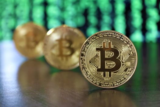 Golden bitcoin coins highlighted against a digital green code background, symbolizing cryptocurrency.