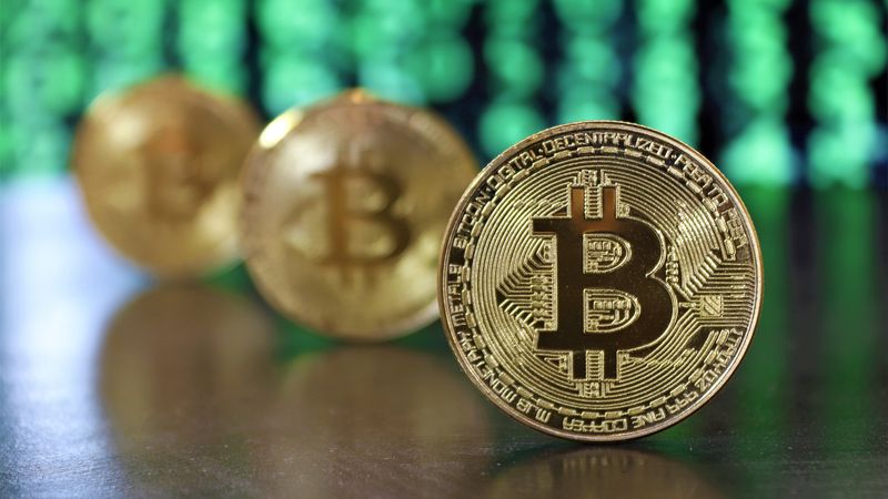 Golden bitcoin coins highlighted against a digital green code background, symbolizing cryptocurrency.