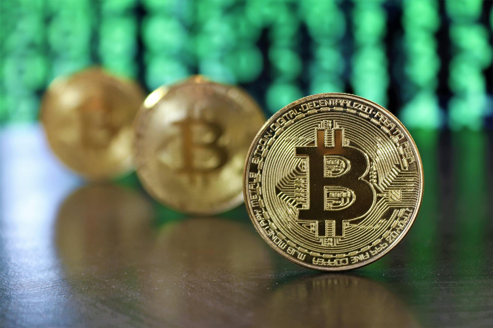 Golden bitcoin coins highlighted against a digital green code background, symbolizing cryptocurrency.