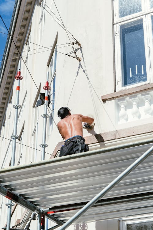 A Shirtless Man Working while Standing on a Scaffolding
