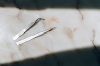 高角度拍摄大理石表面上的两把精密镊子，凸显优雅与简约