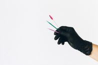 白色背景下，一只黑色手套拿着一把彩色牙刷