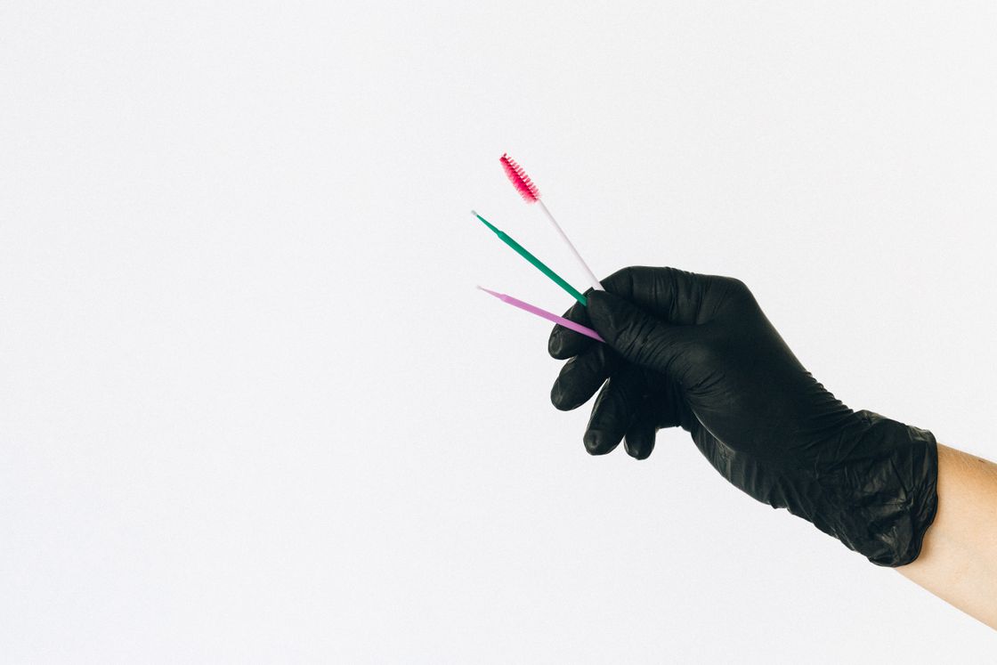 Black-gloved hand holding three small interdental brushes against a white background