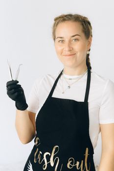 Smiling woman in apron and gloves holding tweezers on a white background.
