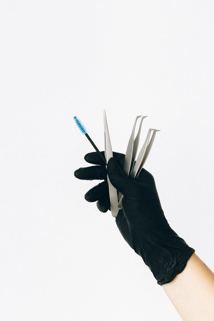 A Hand Holding Tweezers And Mascara Brush