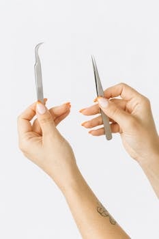 白色背景下，一双手用金属镊子展示美甲