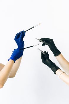 Hands in colorful gloves holding cosmetic tools against a white background.